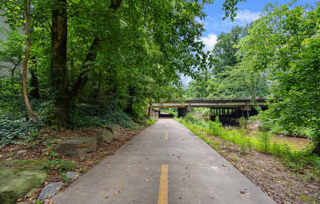 A pathway with a yellow line in the middle leads to a bridge over a river.
