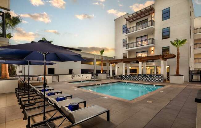 A pool area with sun loungers and a building in the background.