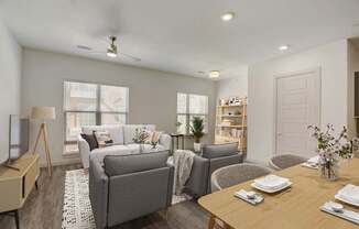 A well-lit living room with a grey couch, a wooden dining table set for two, and a bookshelf filled with books at Infinity on the Point Apartments, Dallas, Texas