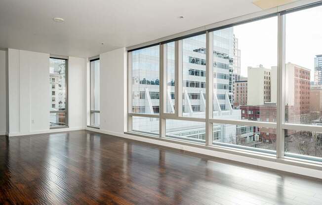 A large empty room with wooden floors and large windows overlooking a cityscape.