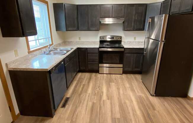 an empty kitchen with wooden floors and black cabinets. Fargo, ND Sheyenne Terrace