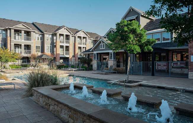 a fountain sits in front of a swimming pool with houses in the background