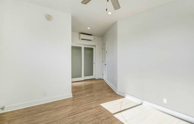 a living room with white walls and wood flooring and a ceiling fan