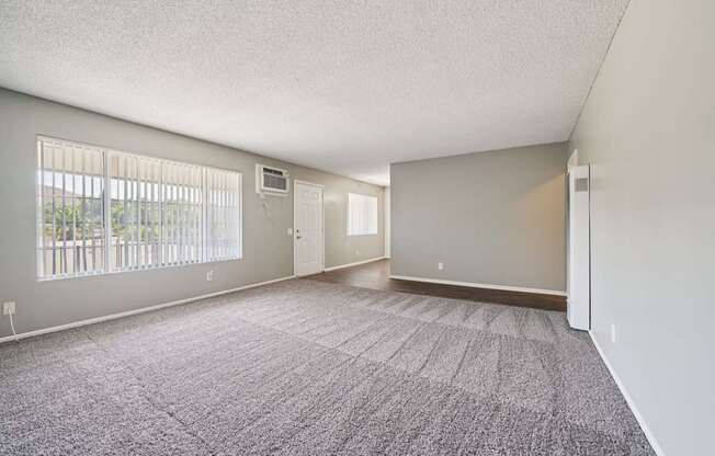 A spacious room with a carpeted floor and a window with blinds.