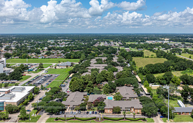 A bird's eye view of a residential area with houses, trees, and a parking lot.