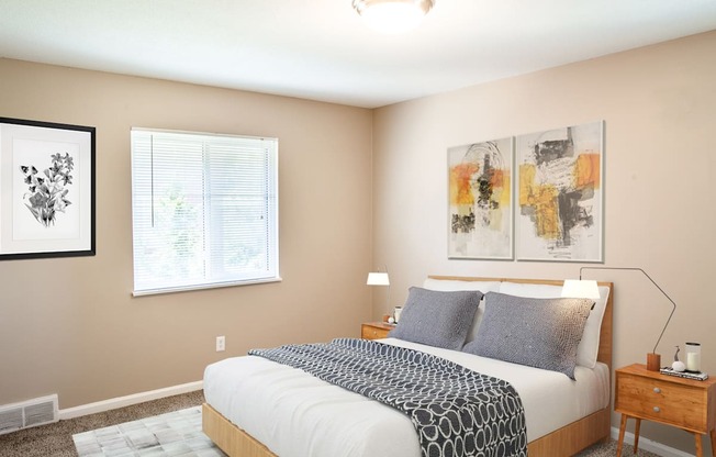 A bedroom with a bed, nightstand, and two paintings on the wall.