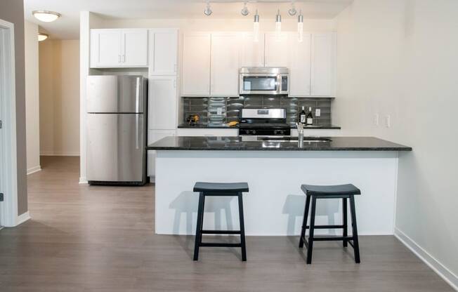 Open floor plan kitchen, with breakfast bar, white cabinet finishes and stainless steel fridge and microwave