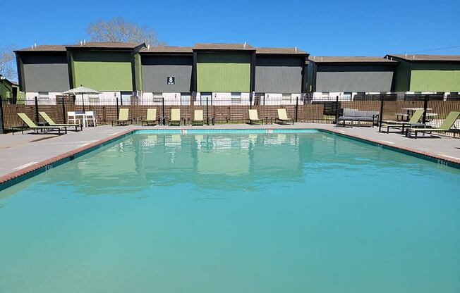 a swimming pool with chairs around it and a building in the background at Ivy Plains at Brooks Apartments, San Antonio , TX