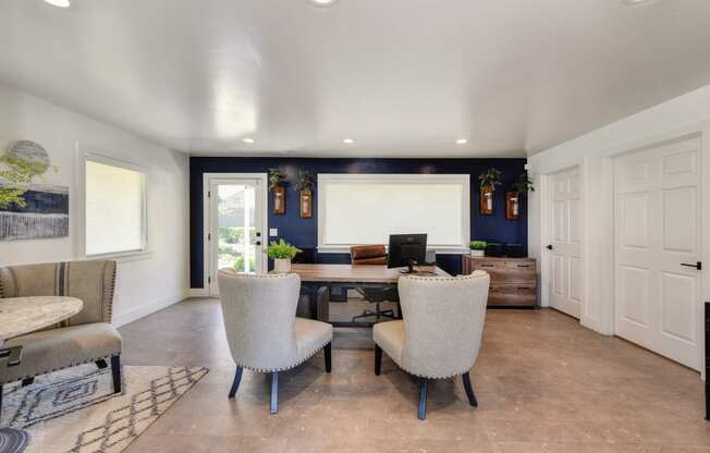 Inside Manager and  Leasing Office. Desk with two chairs in front of it. Additional seating with small round table to the left.