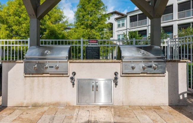 two stainless steel bbq grills on a concrete wall with a sign in the background