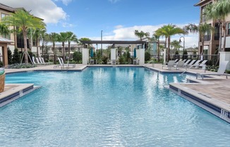 a large swimming pool with chaise lounge chairs and palm trees in the background
