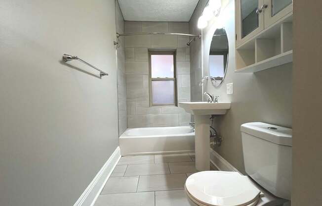 A white toilet sits in a bathroom with a white sink and a white bathtub.