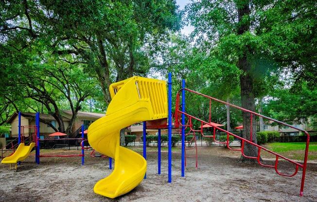 A playground with a yellow slide and red and blue swings.