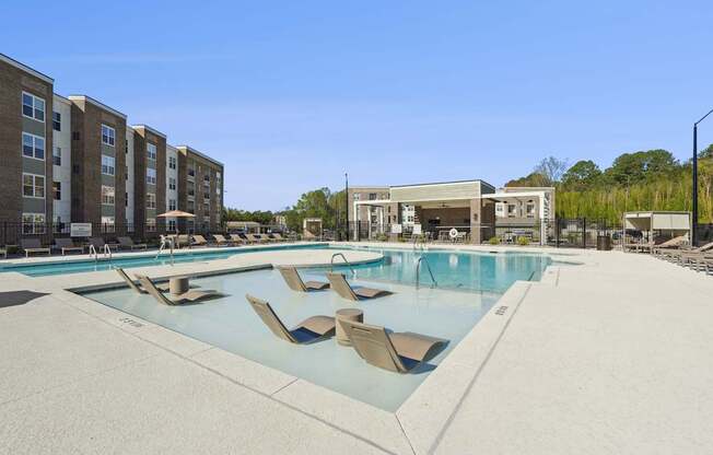 A large swimming pool with lounge chairs in front of apartment buildings.