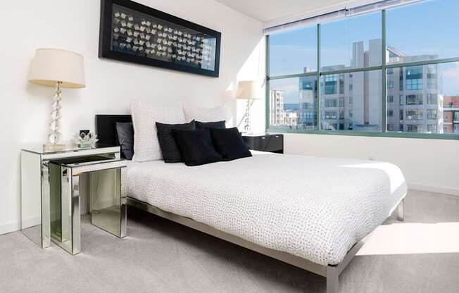 A bedroom with a large bed, a table with a lamp, and a framed picture on the wall.