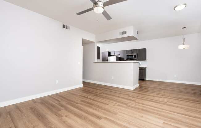 an empty living room with a ceiling fan and a kitchen