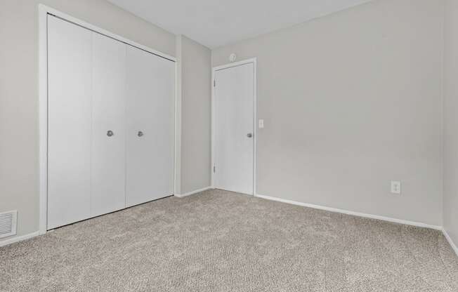 an empty bedroom with white doors and carpeting