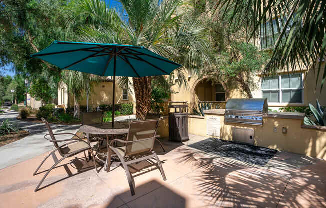 a patio with a grill and a table with chairs and an umbrella