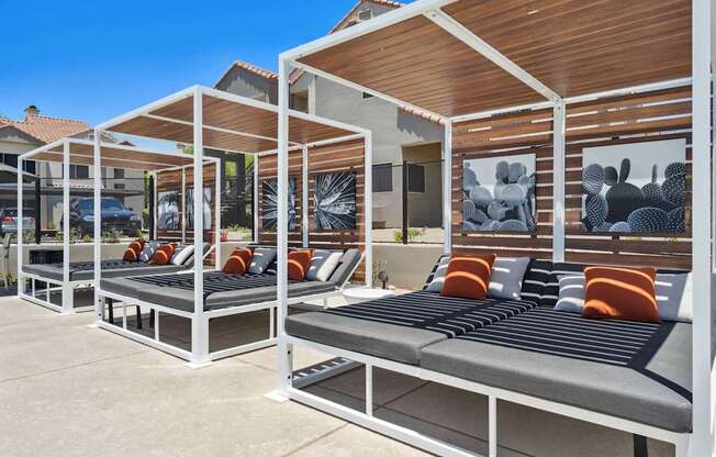 A row of white and grey outdoor beds with orange cushions.