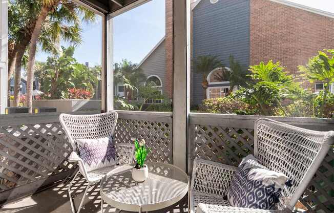 A patio with two chairs and a table with a vase of flowers on it.