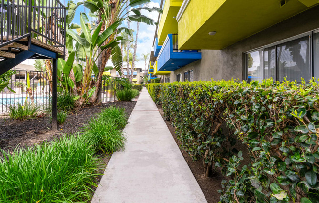 a walkway between two buildings with plants on either side