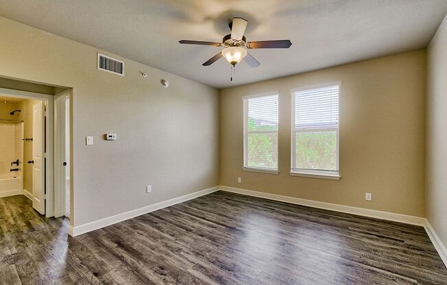 an empty bedroom with a ceiling fan and two windows
