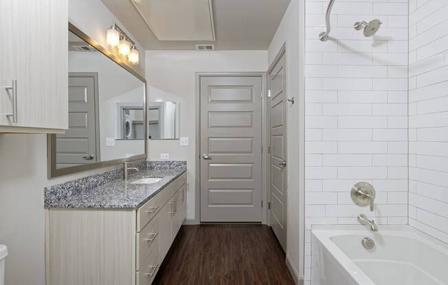 Bathroom with wood floor, granite sink countertop and bathtub with white tiles