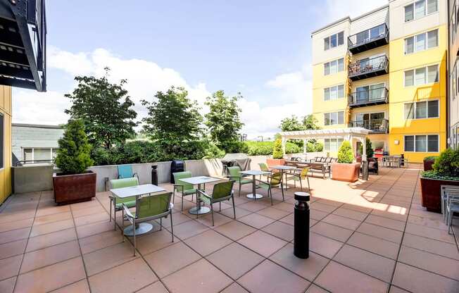 A patio with tables and chairs is surrounded by buildings.