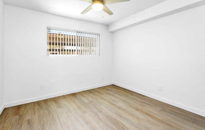 A room with a ceiling fan and a window with blinds.