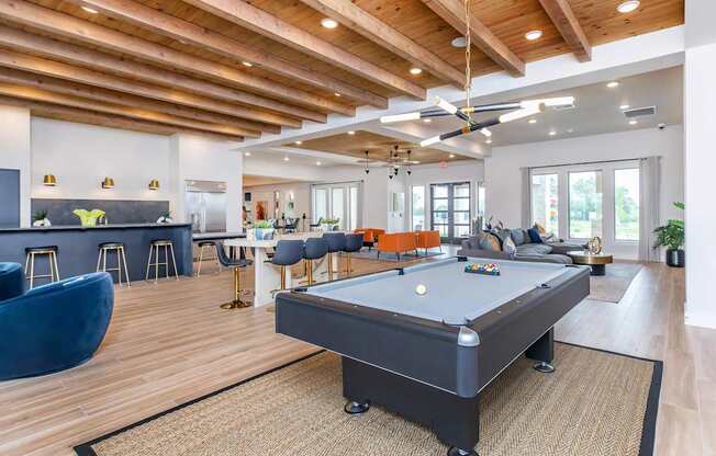 A billiard table is in the middle of a room with a bar and seating area.