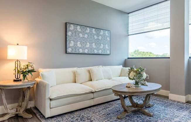 A living room with a white couch, a round table with a vase of flowers, and a framed picture on the wall.