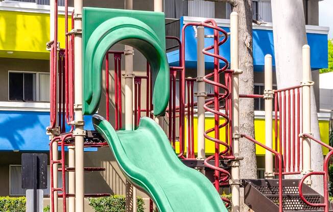 a playground with a green slide in front of a building