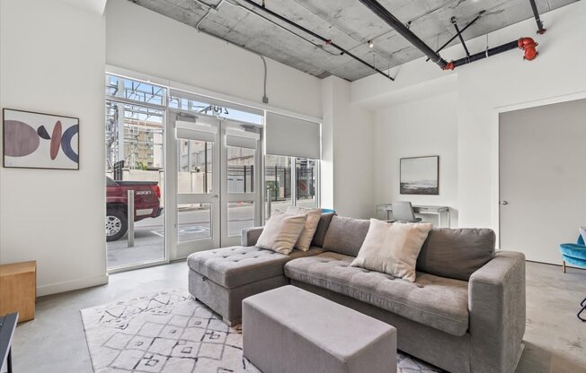 A grey couch with pillows sits in a room with a grey rug and a grey ottoman.