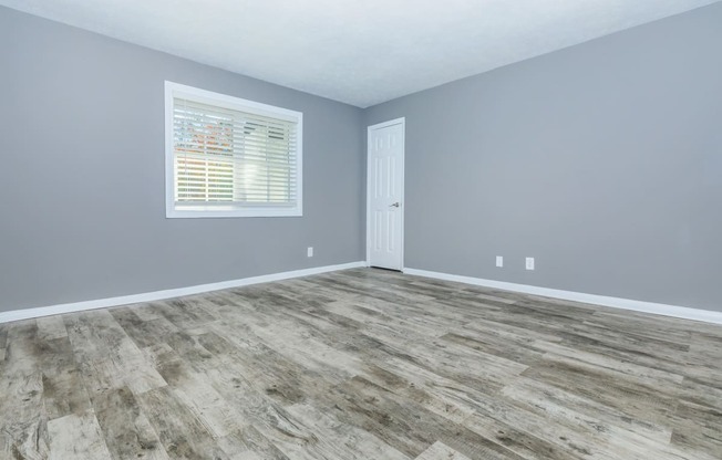 an empty room with wood floors and grey walls and a window