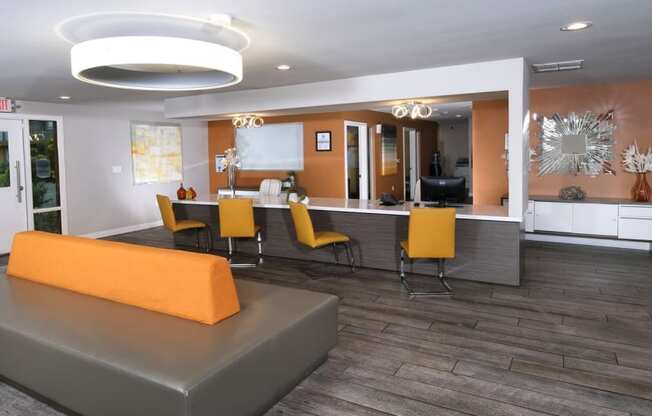 Fifteen 50 apartments Las Vegas clubhouse with modern orange chairs at a bar in front of orange accent wall and grey wood inspired flooring.