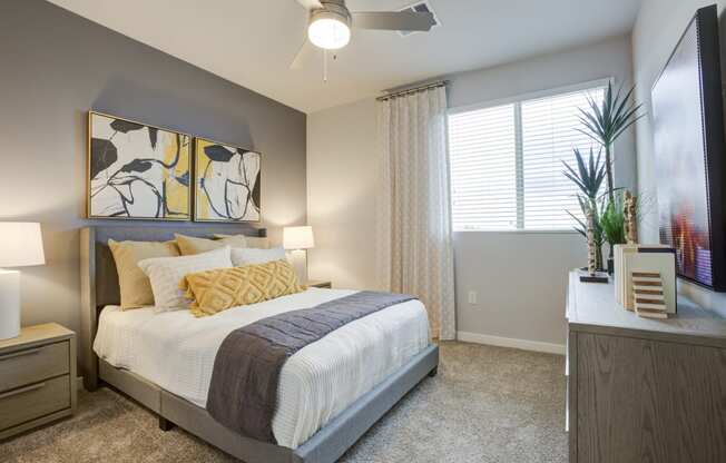 South Scottsdale Apartments - Lucent Scottsdale - Spacious Bedroom With Carpeted Flooring, Bed, Side Tables With Lamps, Dresser, Ceiling Fan, And A Window With Blinds