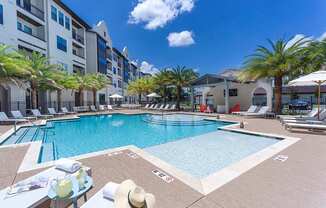 a swimming pool with chaise lounge chairs and palm trees in front of an apartment building