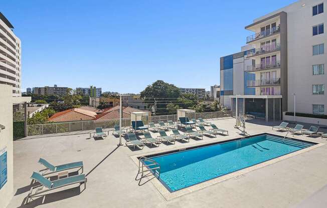 1- & 2-Bedroom Apartments for Rent in Miami, FL – Riverview One Apartments – A swimming pool with sun loungers and apartment buildings in the background.