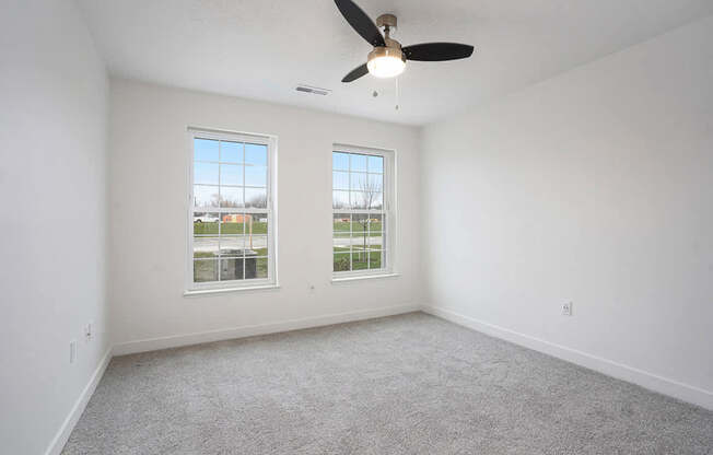 A spacious bedroom with a ceiling fan and two windows at Meadowbrooke Apartment Homes in Kentwood, MI 49512