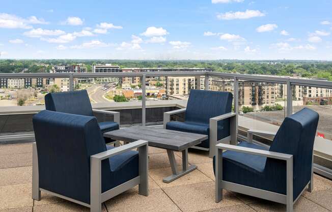 an outdoor patio with blue chairs and a wooden table with a view of the city