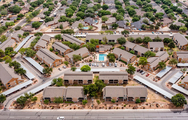 Aerial view of the Trinity Place apartment community showing multiple residential buildings arranged around a central pool area. Tree-lined walkways, covered parking, and landscaped courtyards connect the property, while nearby streets and surrounding neighborhoods highlight the convenient community layout.