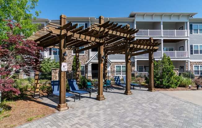 a patio with a pergola and chairs in front of an apartment building