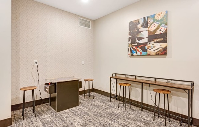 a room with a desk and stools and a painting on the wall