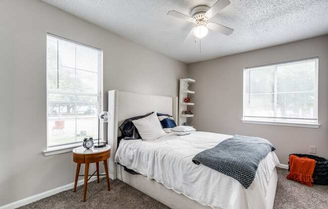 a bedroom with a bed and a ceiling fan and two windows