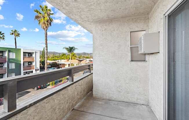 A balcony with a concrete floor and wall with a window and air conditioning unit.