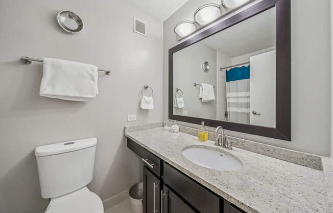 A bathroom with a toilet, sink, mirror, and towel rack.