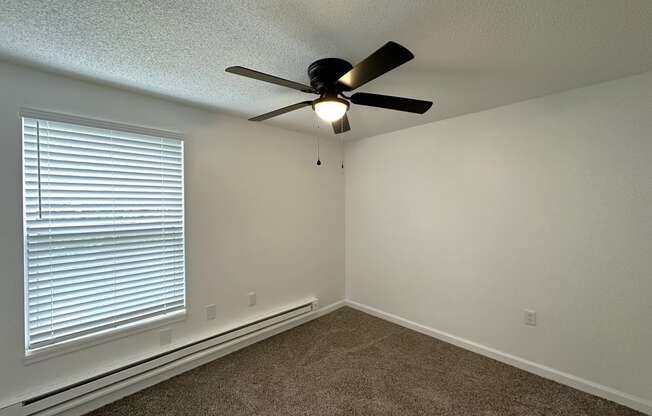 a bedroom with a large window and a ceiling fan