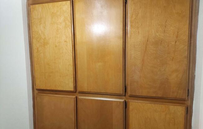 A wooden cabinet with multiple doors in a simple design. The finish is light-colored, showcasing a smooth texture with visible wood grain. The cabinet has a clean and minimalist appearance, suitable for storage in a kitchen or utility space.