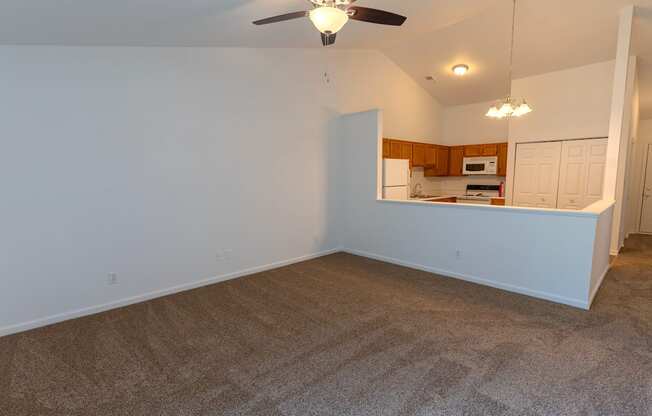 an empty living room with a ceiling fan and a kitchen