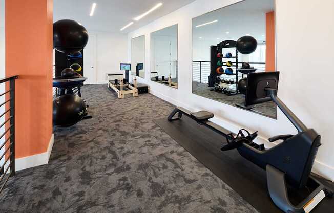 A gym with a rowing machine, exercise balls, and mirrors.